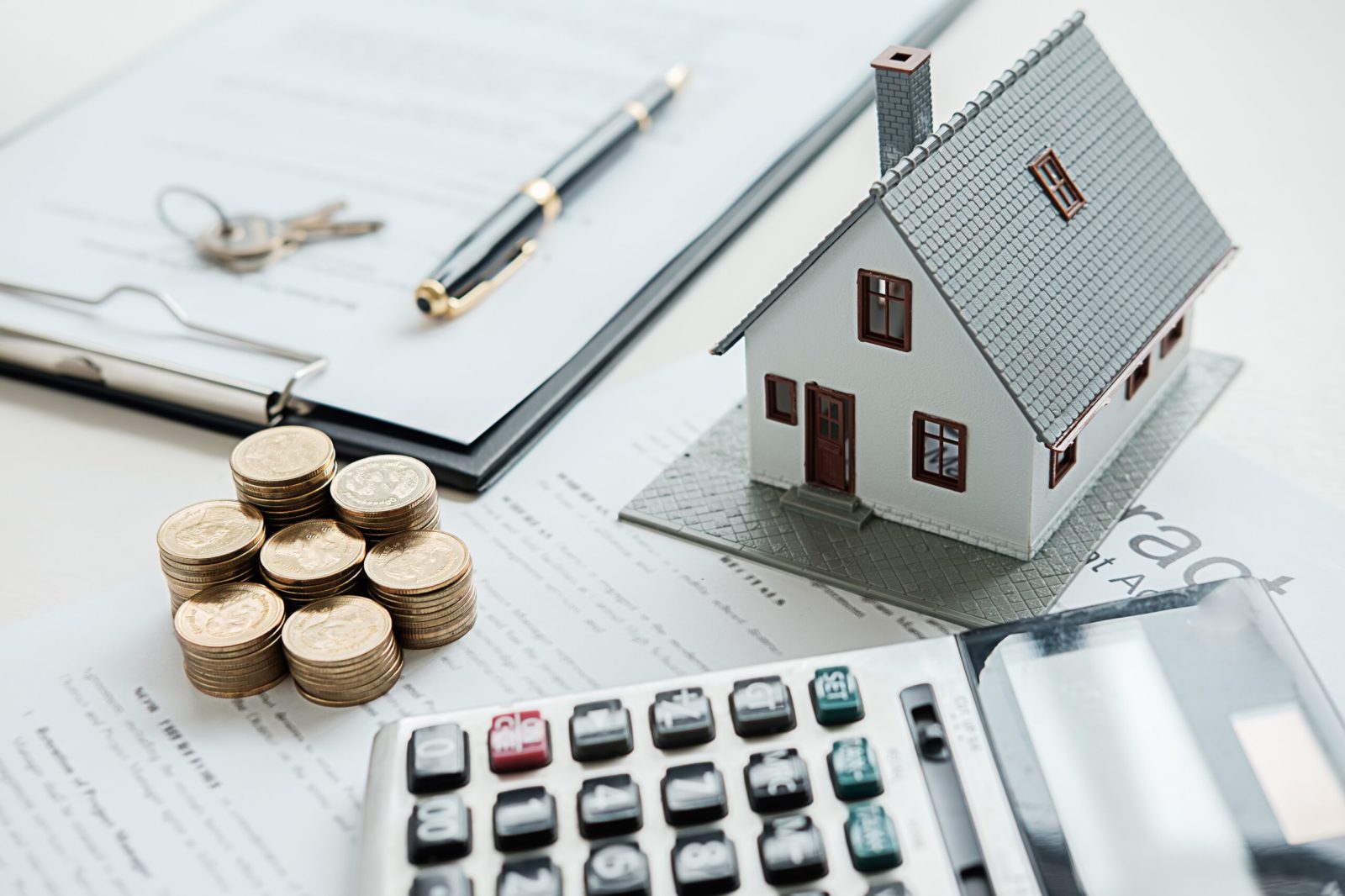 Miniature house on a desk beside coins and a calculator, symbolising financial and mortgage matters