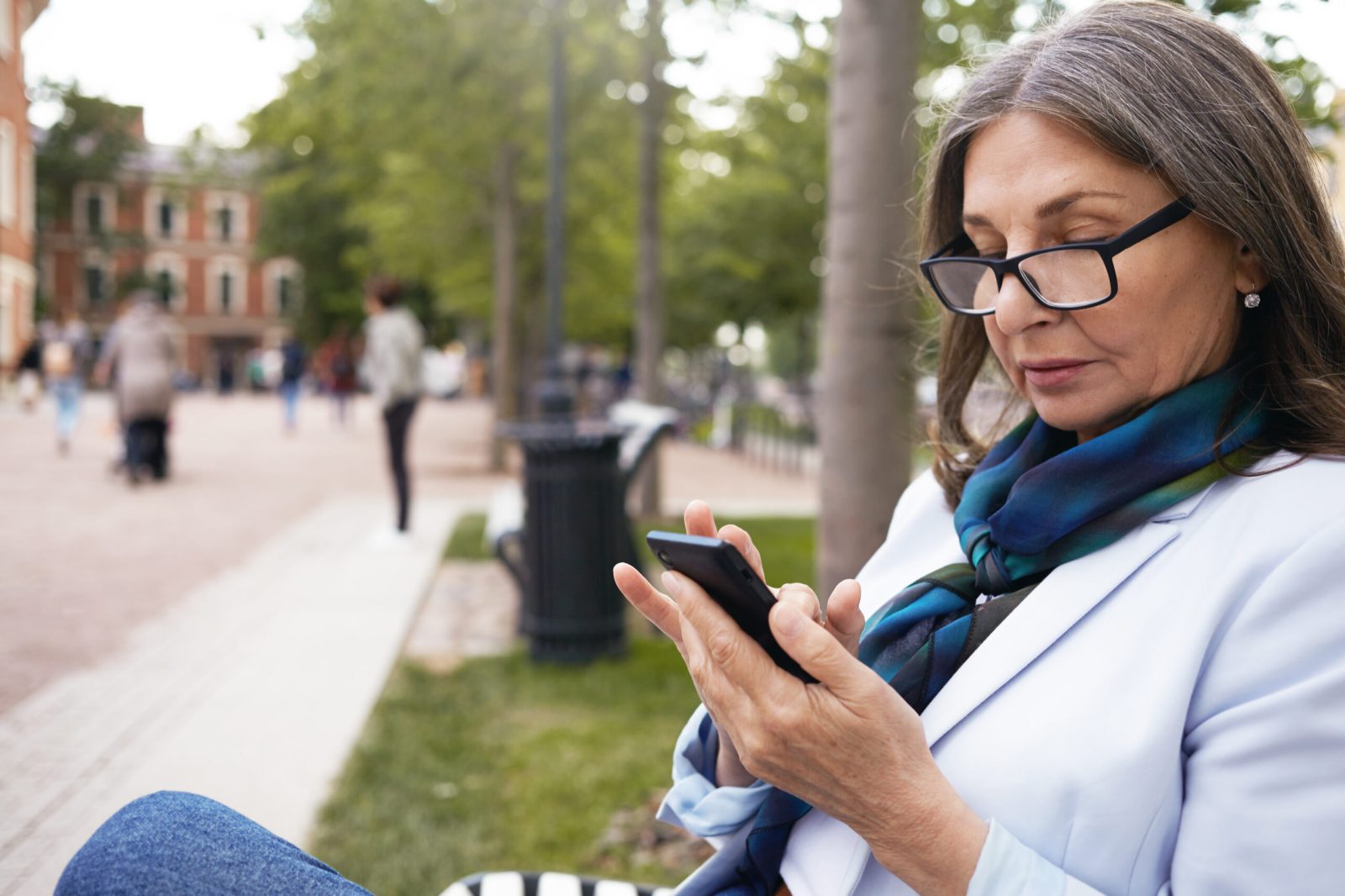 Woman in her 50s reviewing financial documents on a phone at the park.