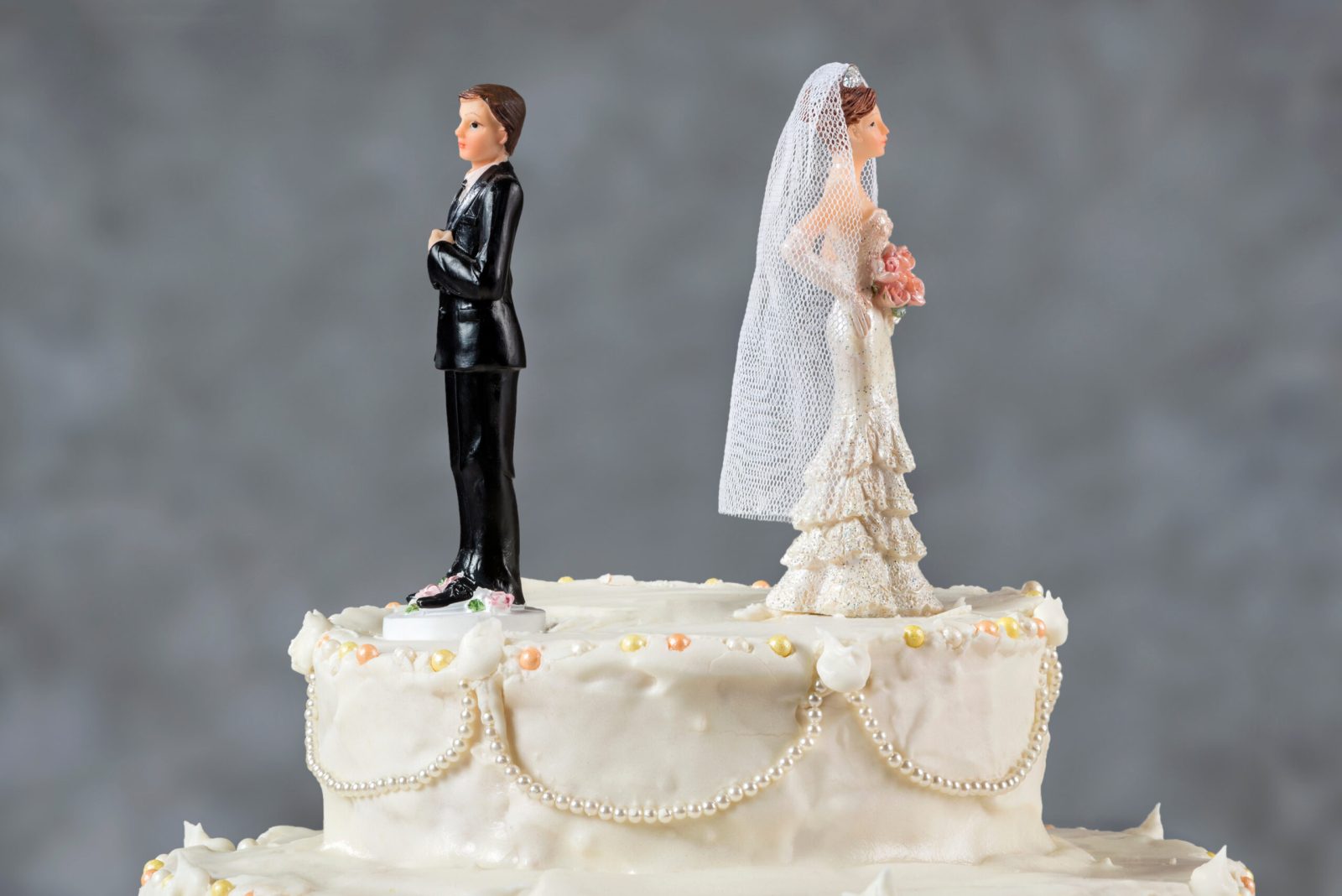 Separated bride and groom wedding cake toppers facing away on a cut wedding cake