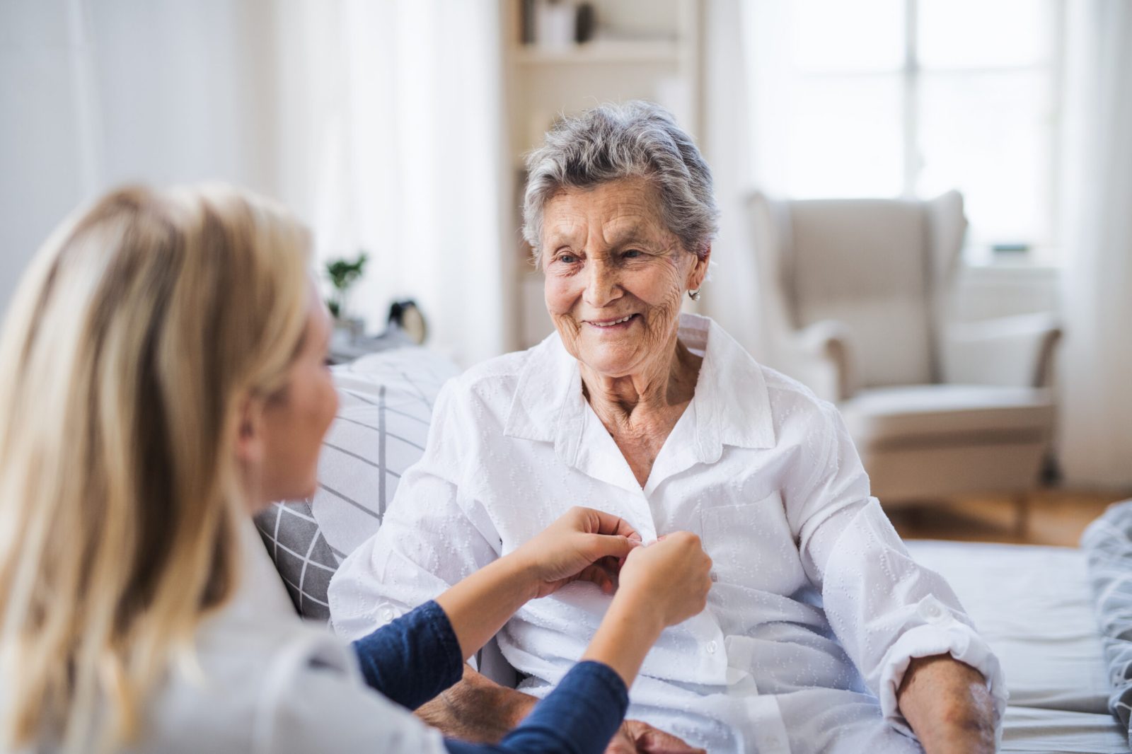 Elderly woman receiving assistance with clothing from a younger caregiver