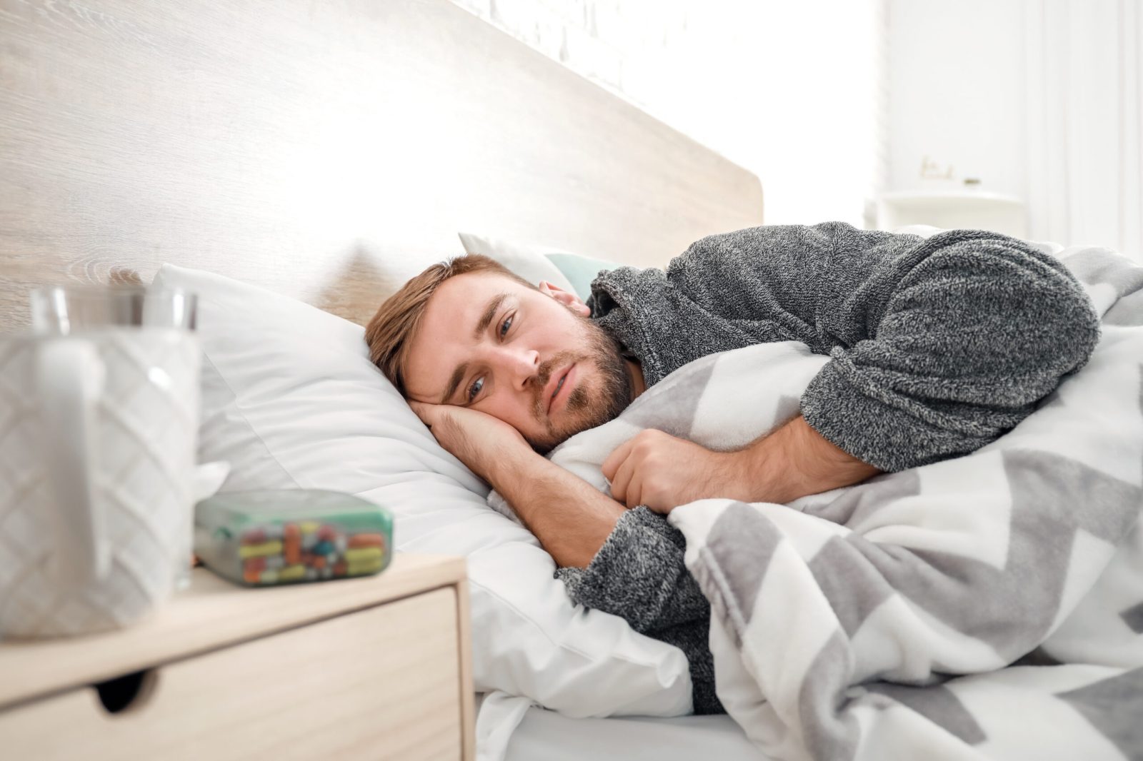 Man in bed wearing a dressing gown with tablets and a mug on the bedside table