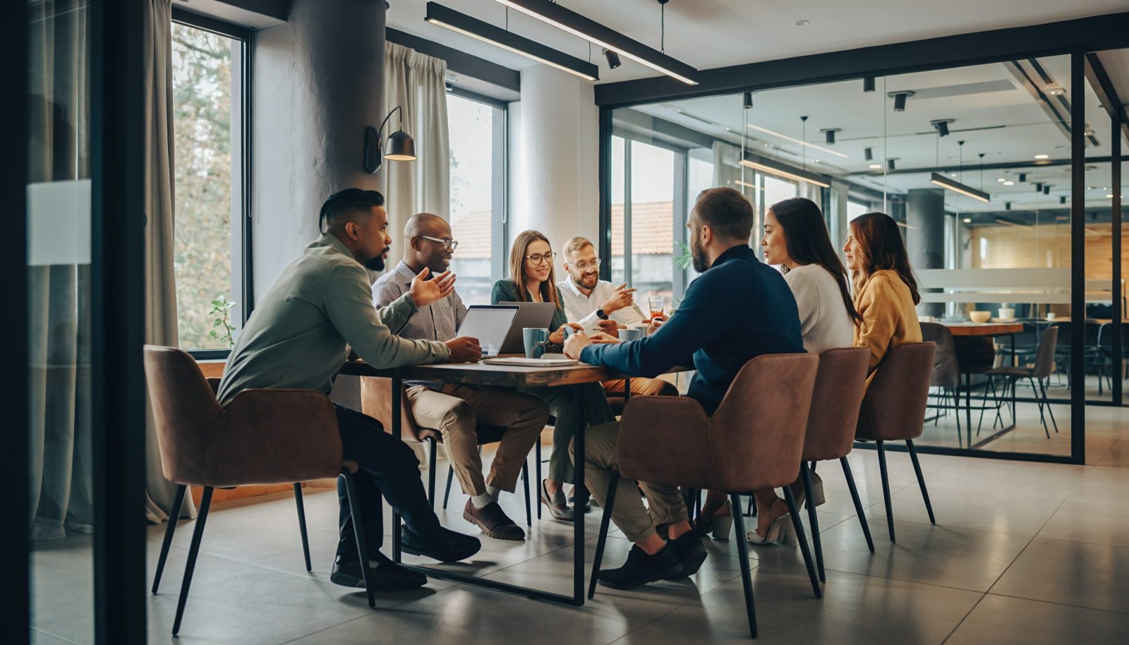 Diverse group of staff seated around a meeting table in a modern office, discussing documents in a professional setting.