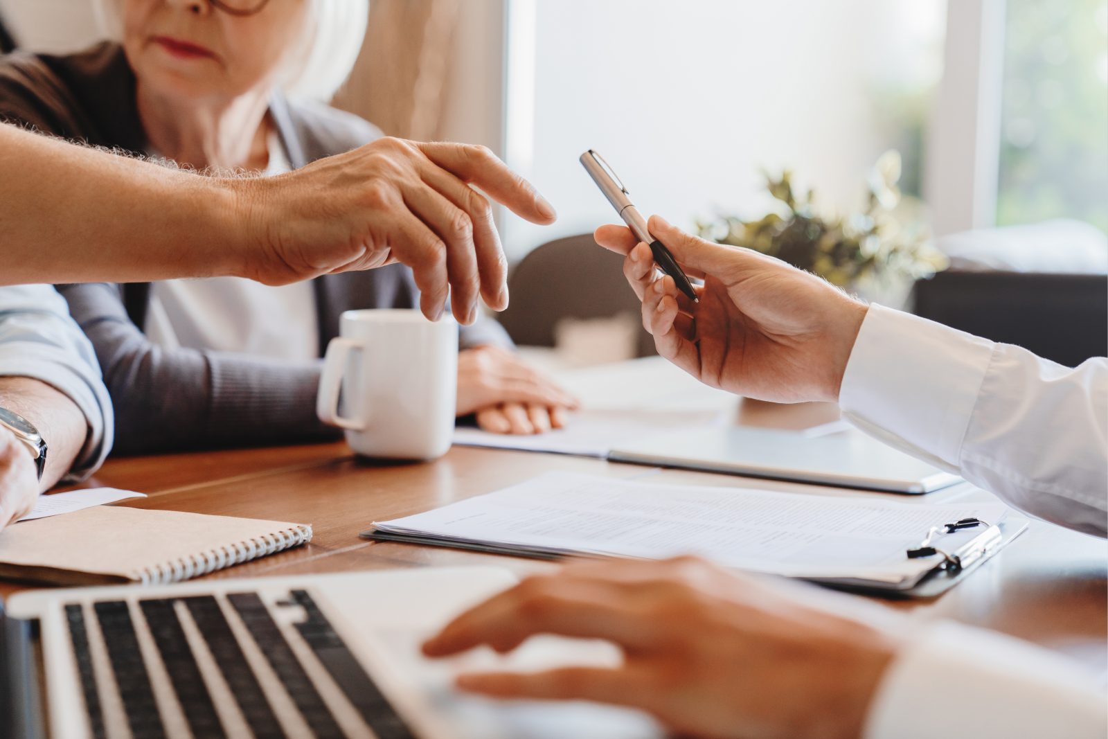 Man reaching for pen at table, assisted by solicitor, wife beside him